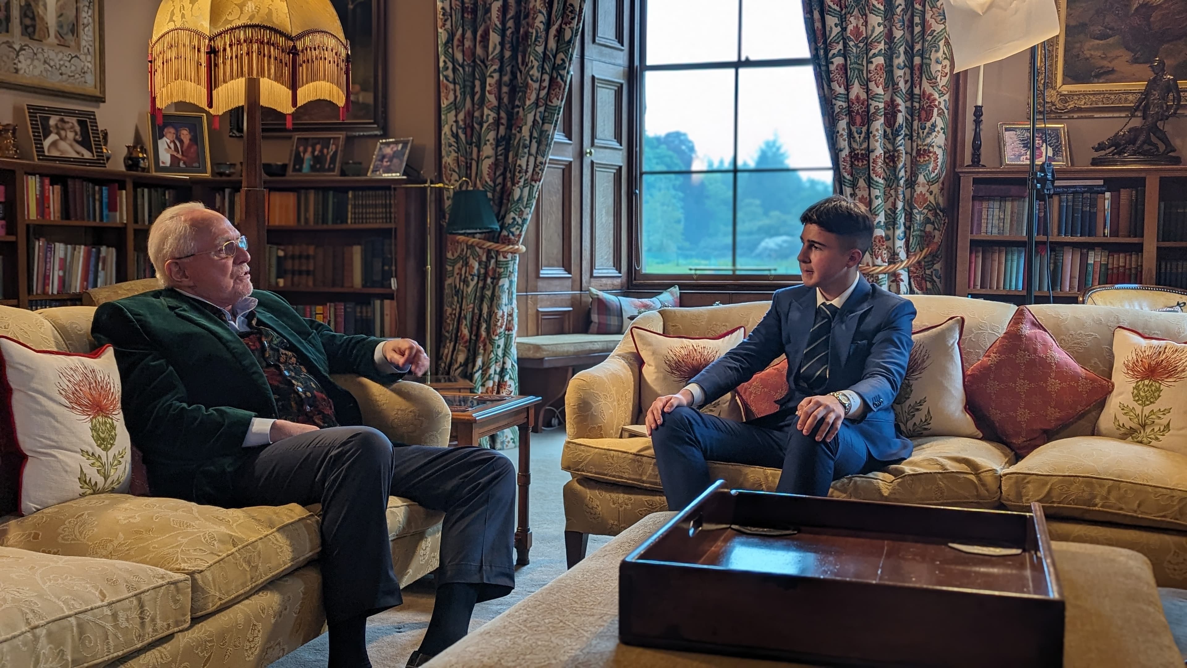 An older man in a green jacket talks with a young man in a blue suit.